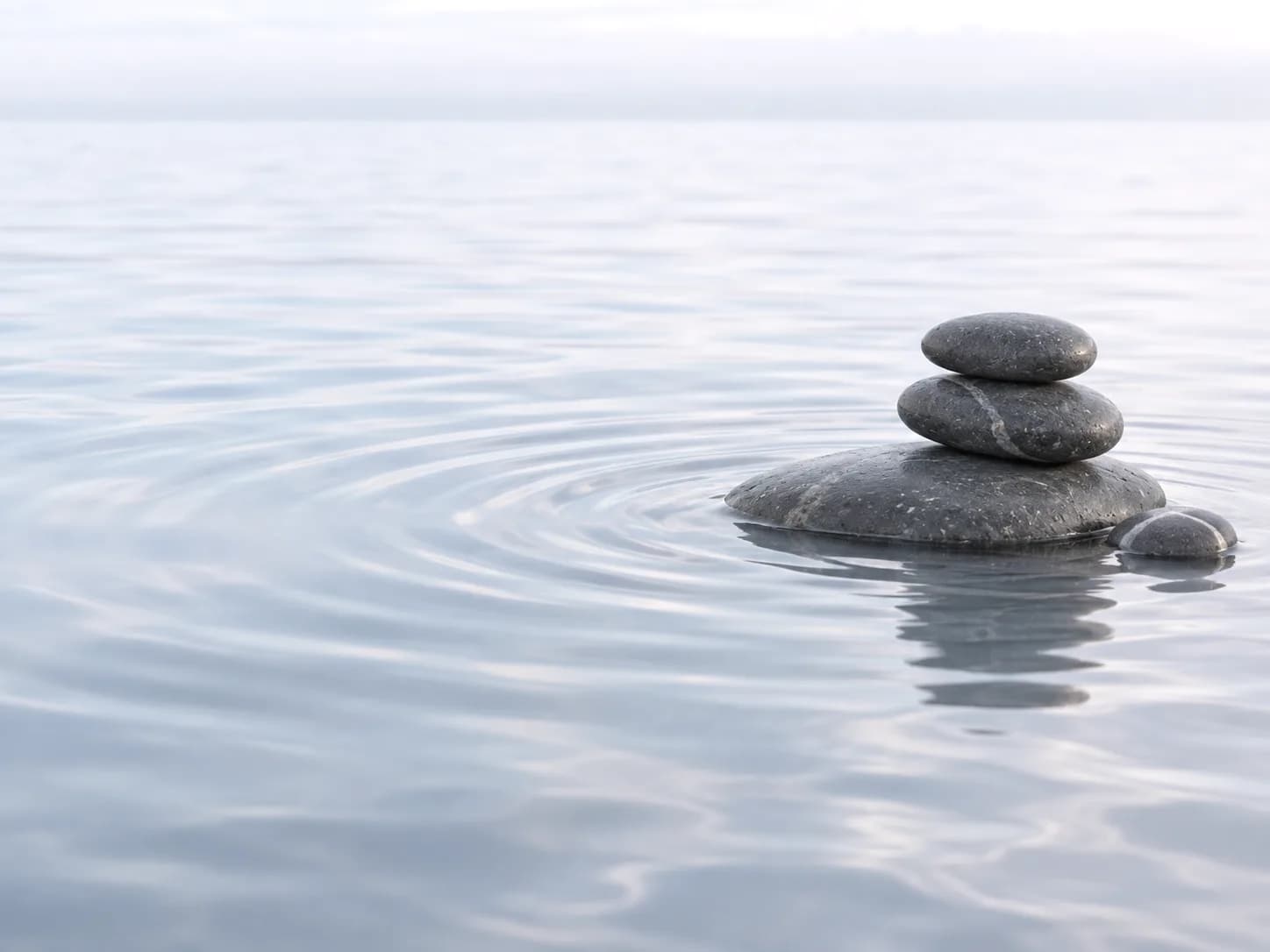 A small stack of stones resting in still water, with ripples spreading out around it